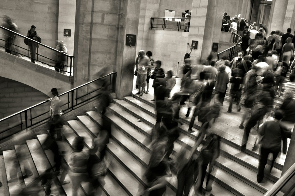 a black and white image of a busy stairway with lots of people. Some people are blurred as their motion was captured by the camera.